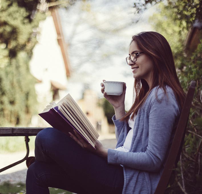 A woman reading with a cup of tea in a garden